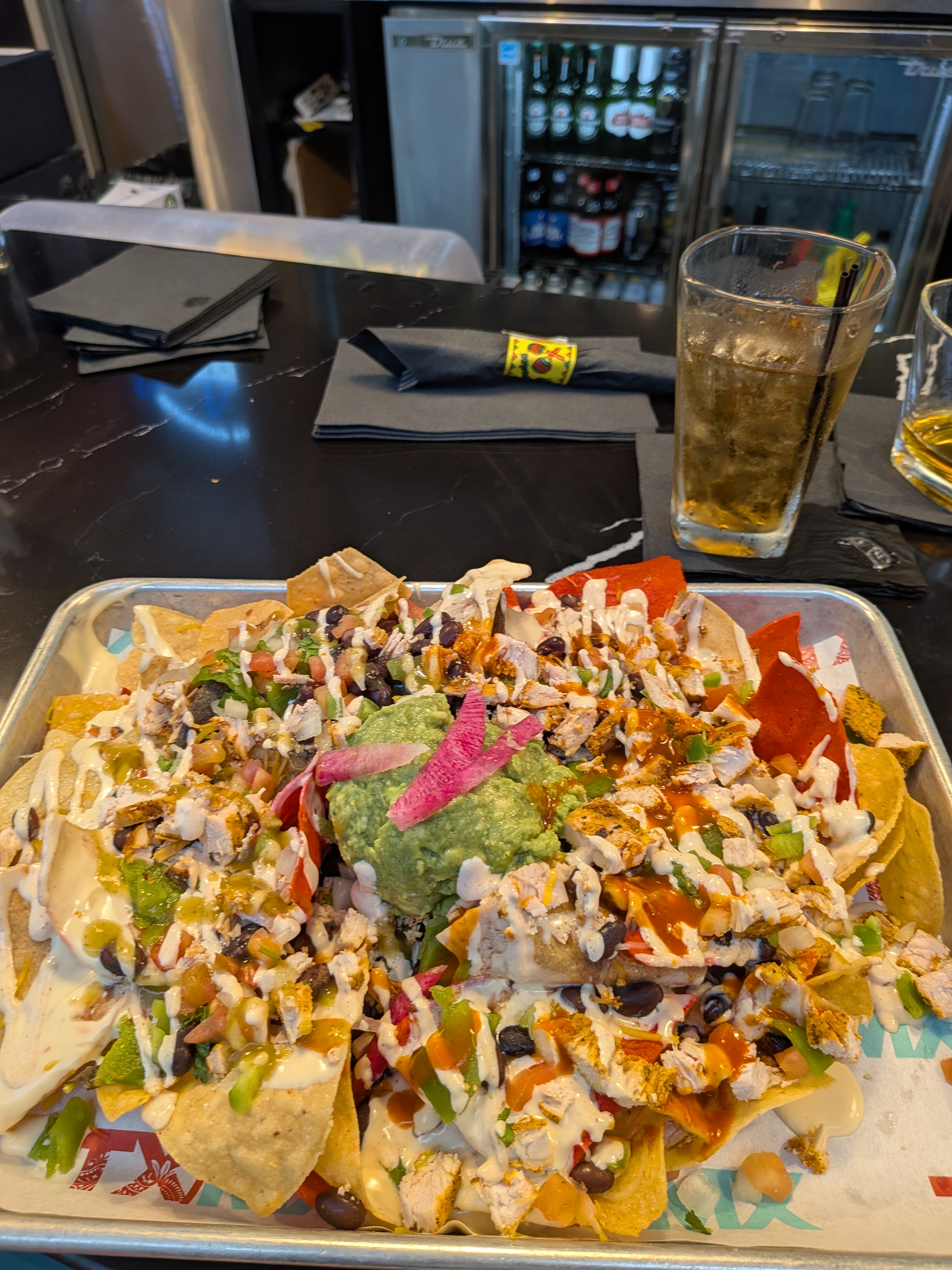 A tray of loaded nachos with chicken, black beans, guacamole, and queso on a bar counter