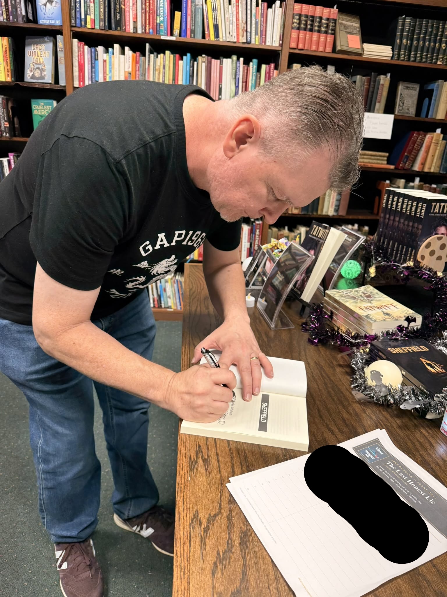 Charles signing a copy of Sheffield at a table in Basement Books KC, with copies of Tatwitt and Sheffield on display