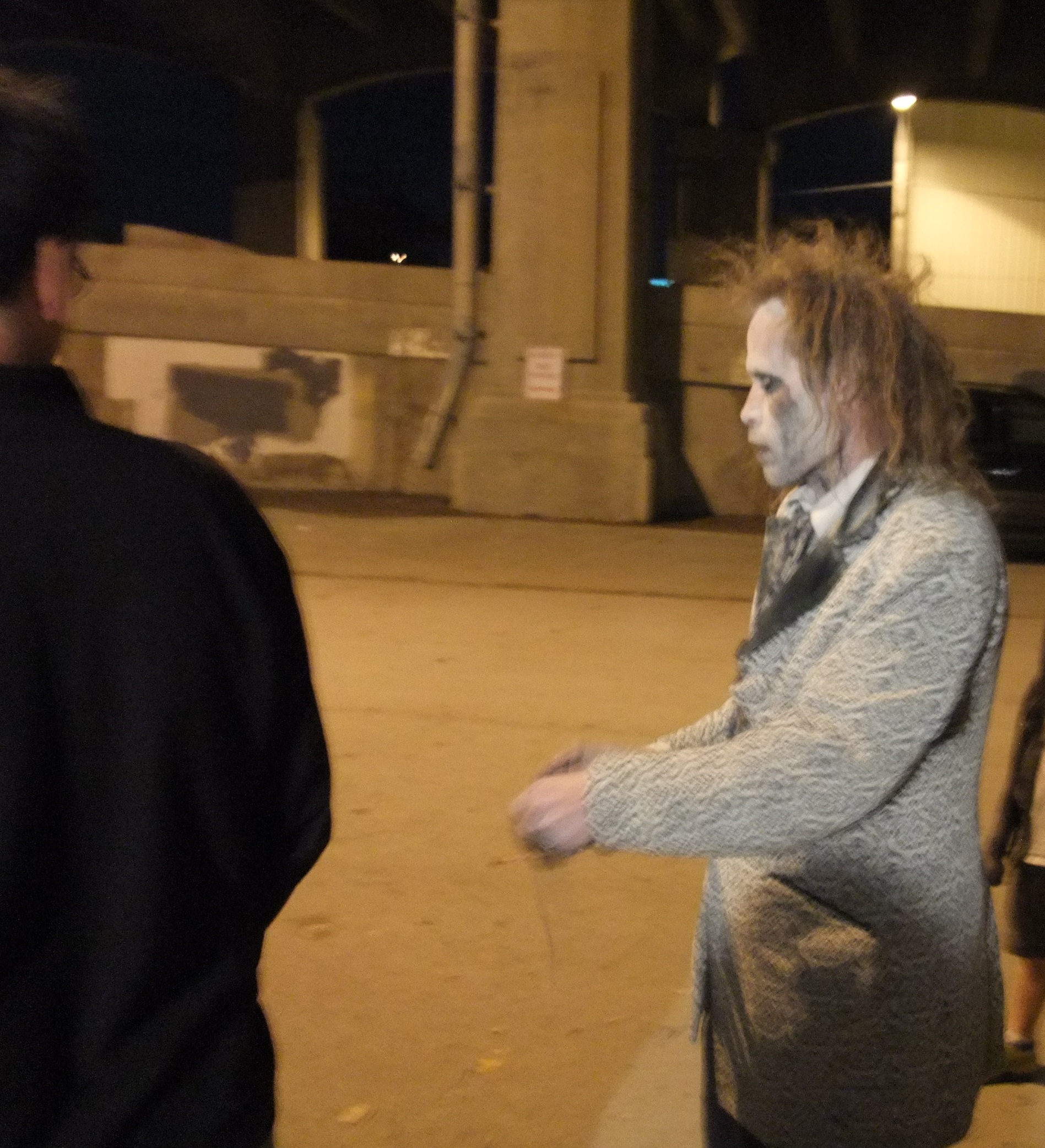 A performer in white face paint and a ragged grey coat outside The Edge of Hell